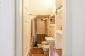 Un bagno stretto con doccia, WC e lavandino.