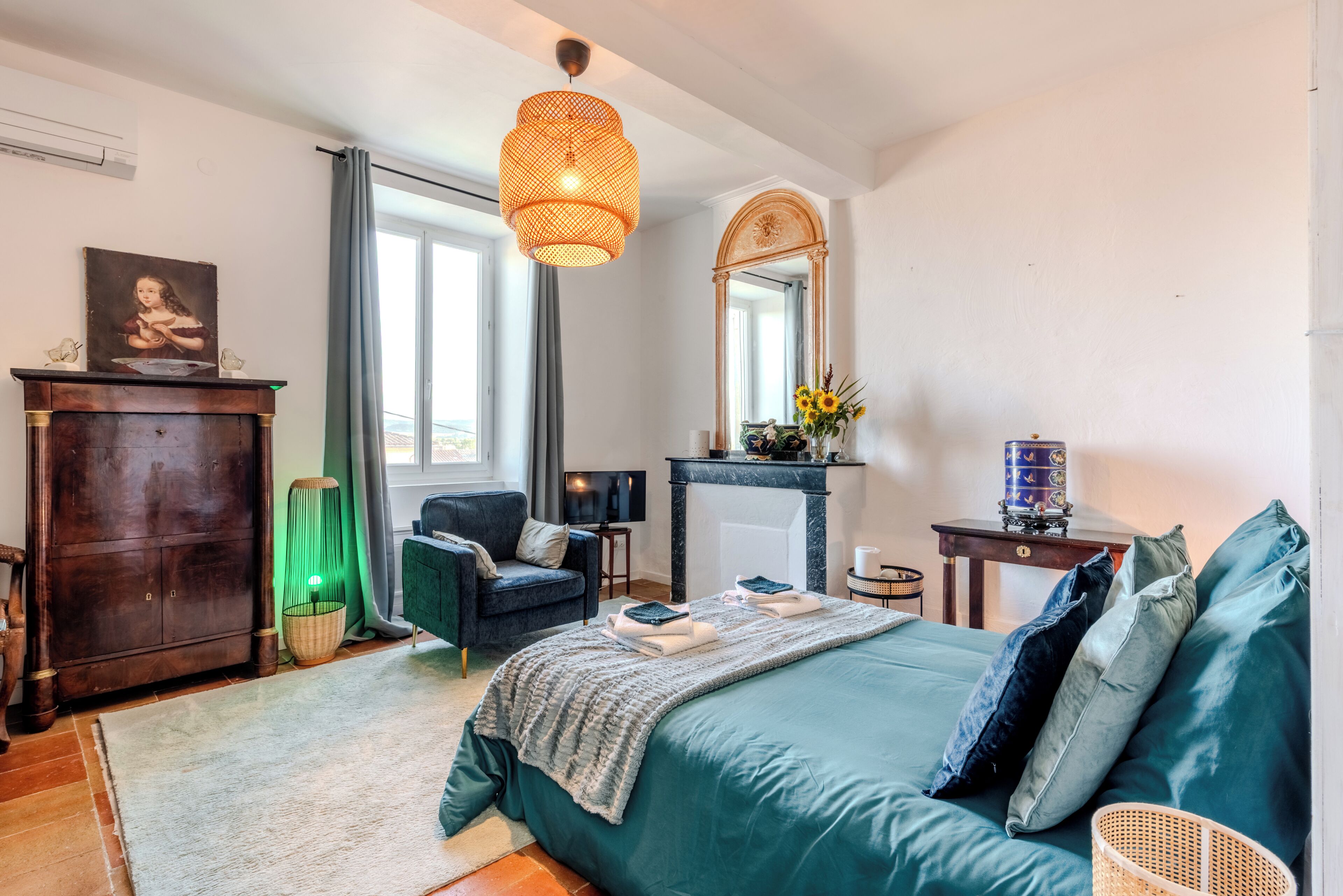 Ein Schlafzimmer mit einem Bett, einem Schminktisch, einem Sessel, einem Spiegel, einem Kamin und einem Fernseher.