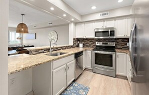 A modern kitchen with white cabinets, stainless steel appliances, and a granite countertop.