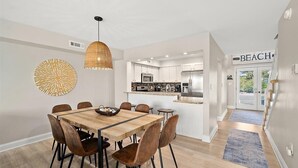Eine moderne Küche mit Edelstahlgeräten, ein Essbereich mit Holztisch und -stühlen sowie ein Schild, das einen Strandort anzeigt.