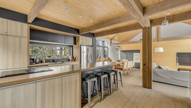 Una cocina moderna con vigas de madera, una zona de bar con taburetes y un espacio comedor con sofá.