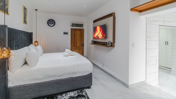 A modern bedroom with a bed, a TV, a clock, and a door. - Boutique Hotel-Style Room In Ferndale-C3 (Randburg)