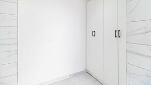 A corner of a room with white marble walls and floor, featuring a large white wardrobe with black handles. - Boutique Hotel-Style Room In Ferndale-C3 (Randburg)