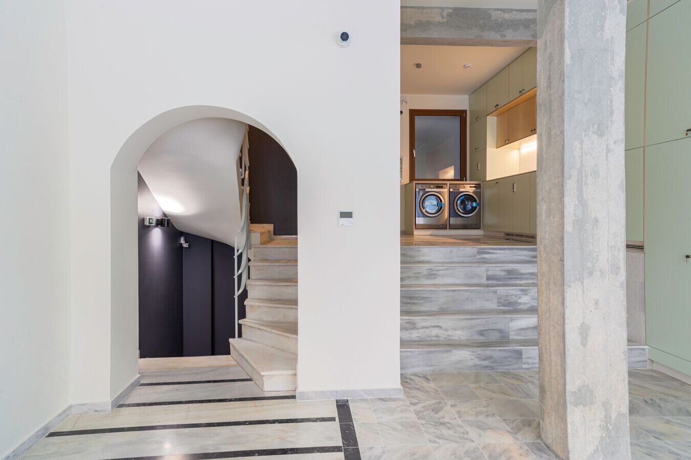 A modern interior with a staircase, a washing machine, and a large arched doorway.