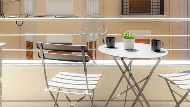 A balcony with a table, two chairs, a potted plant, and a railing. - Exarchia - Apartment for 4 pax (Athina)