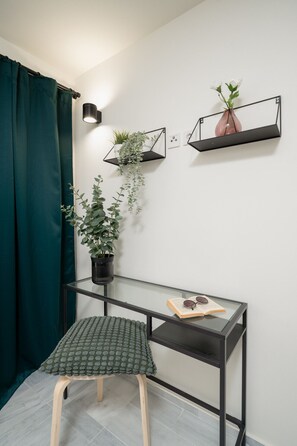 A corner room with a desk, a stool, a potted plant, and a wall-mounted shelf with a plant. - Mooeve Exarchia - Roomy Apartment for 5 pax (Athina)
