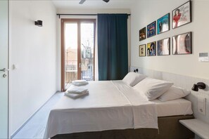 A hotel room with a bed, a window with a view, a wall with framed pictures, and a door. - Mooeve Exarchia - Roomy Apartment for 5 pax (Athina)