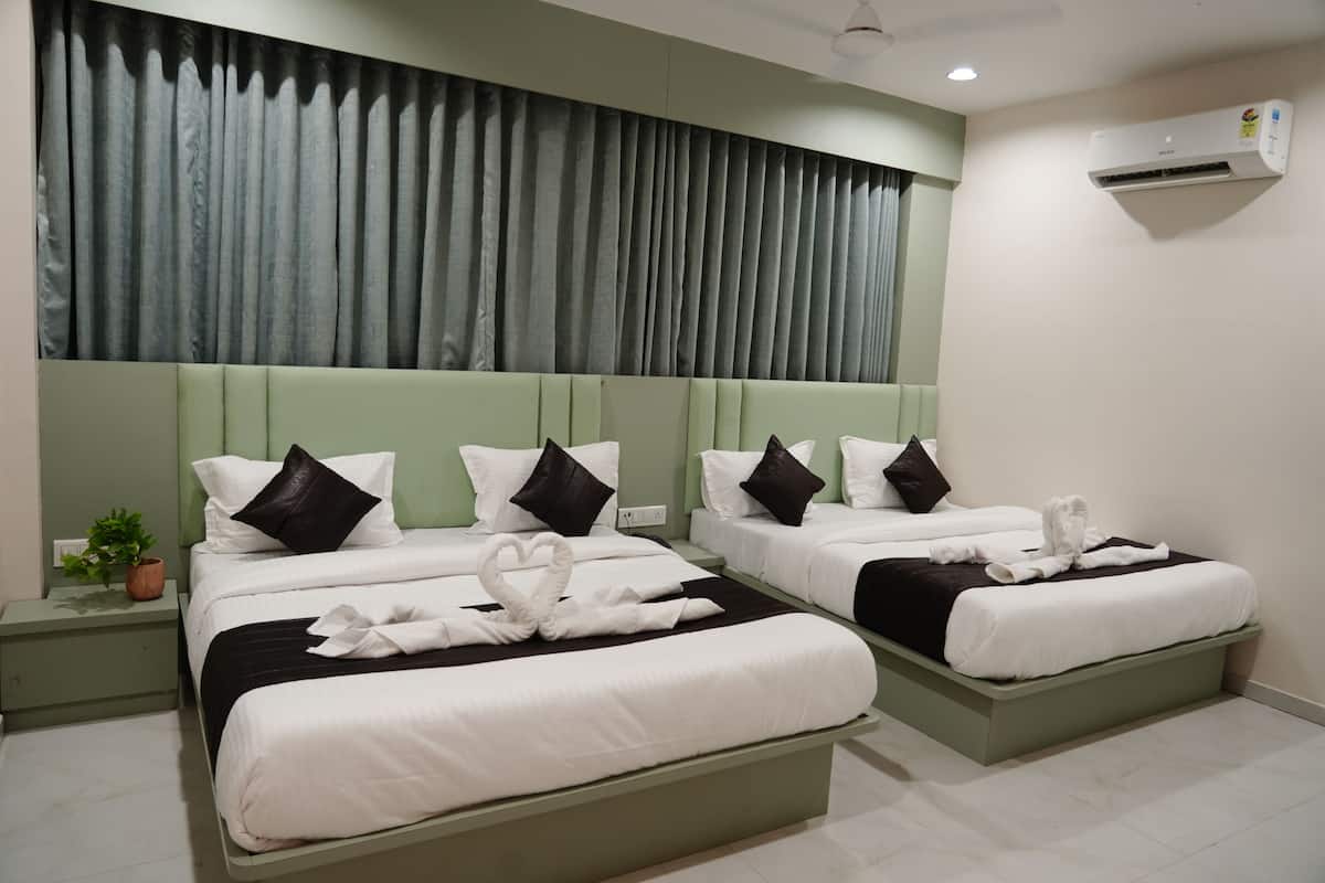 Une chambre d’hôtel avec deux lits, une tête de lit verte, du linge de lit blanc et une décoration en forme de cœur faite avec une serviette.