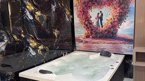 A spa room with a large bathtub, a heart-shaped floral decoration on the wall, and a ceiling with a unique black and gold design.