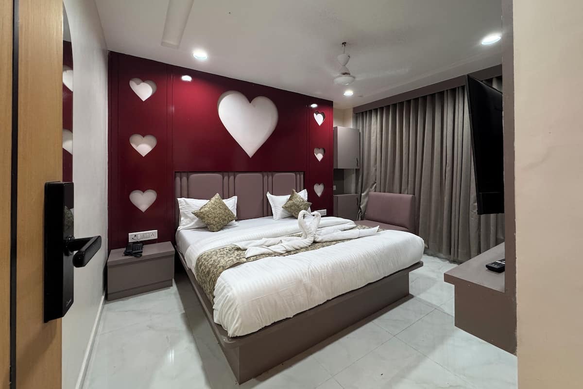 Une chambre à coucher avec un lit, des tables de chevet, une télévision et une grande fenêtre avec des rideaux.
