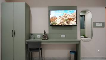 Quarto com escrivaninha verde, televisão montada acima, cadeira, pequena estátua e espelho na parede.