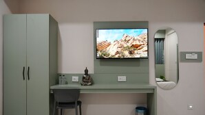 A room with a green desk, a chair, a television mounted above the desk, a small statue, and a mirror on the wall.
