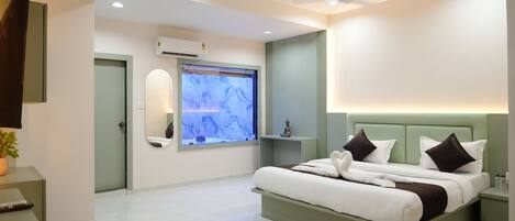 A modern hotel room with a large bed, a wall-mounted TV, an air conditioning unit, and a ceiling fan.
