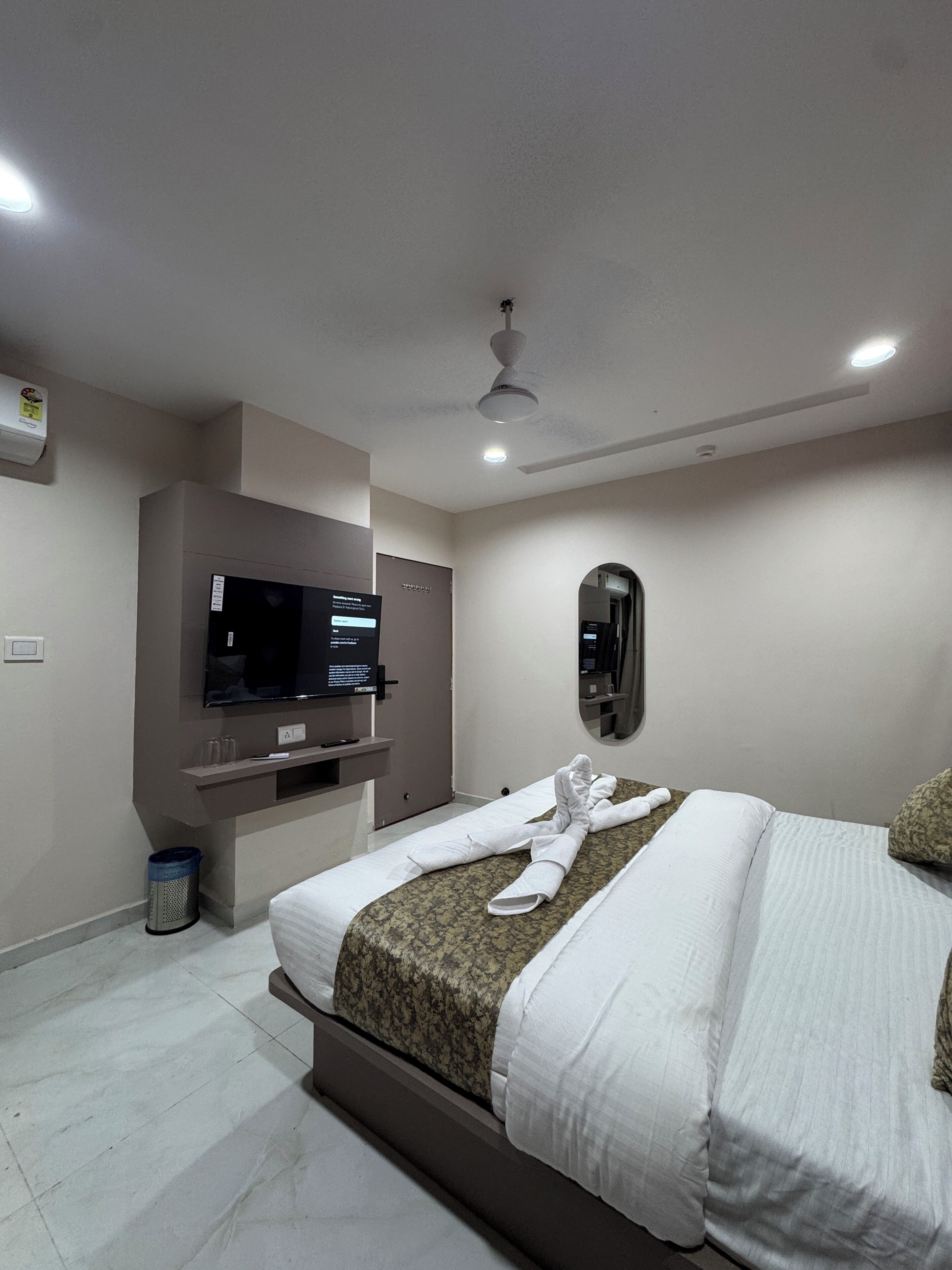 A hotel room with a bed, a television, a ceiling fan, and a trash bin.