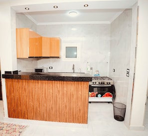 Une cuisine compacte avec des meubles de rangement en bois, un four à micro-ondes, une cuisinière à gaz et une petite fenêtre.