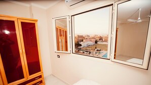 A bedroom with a bed, a wardrobe, and a window with a view of buildings and a pool. - signature house luxor (Luxor)
