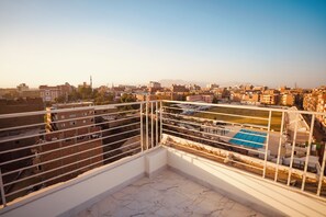 Un balcón con vista a un paisaje urbano, que incluye edificios y una piscina.