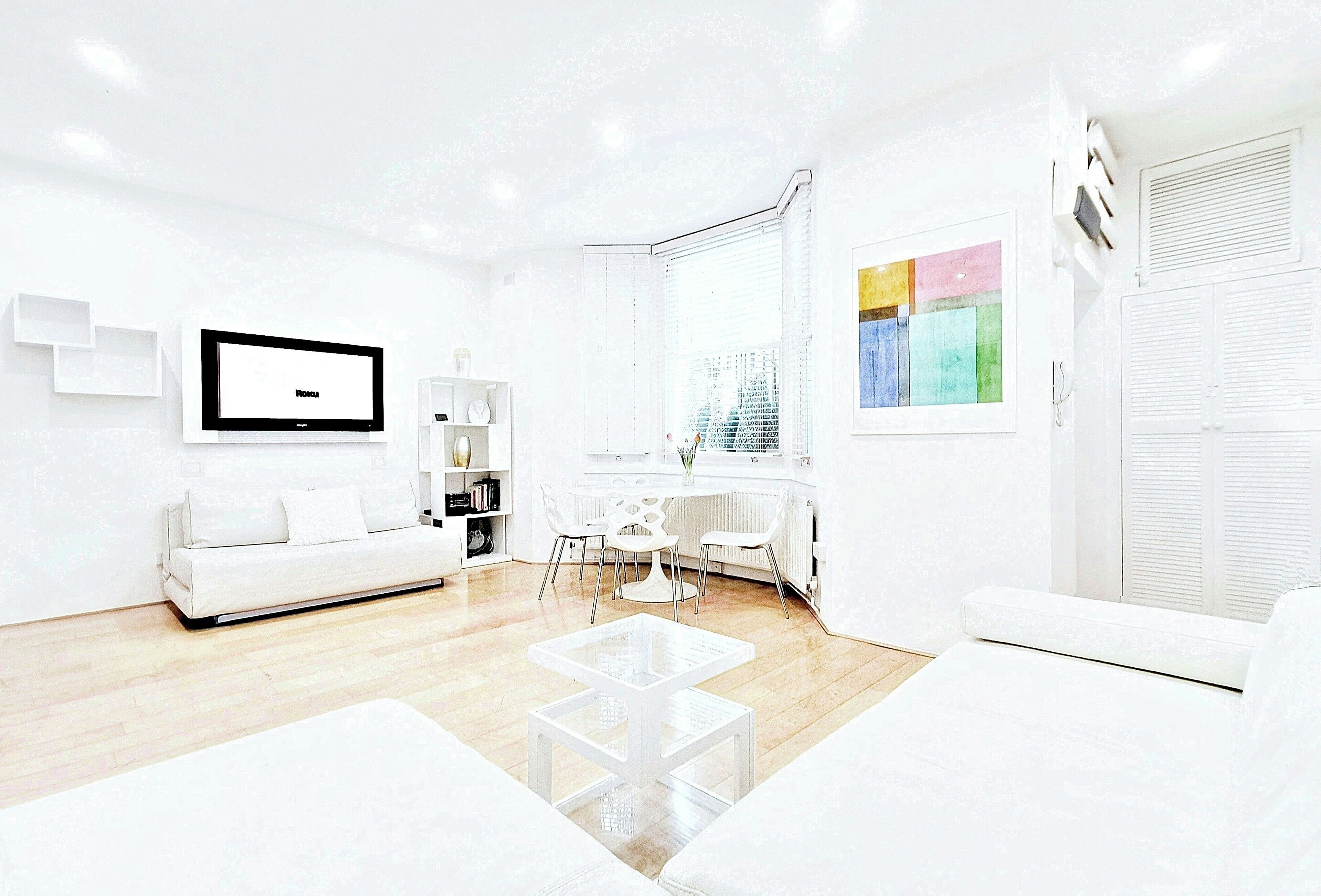 A modern living room with a white sofa, a glass coffee table, a TV, and a dining area with chairs and a table.