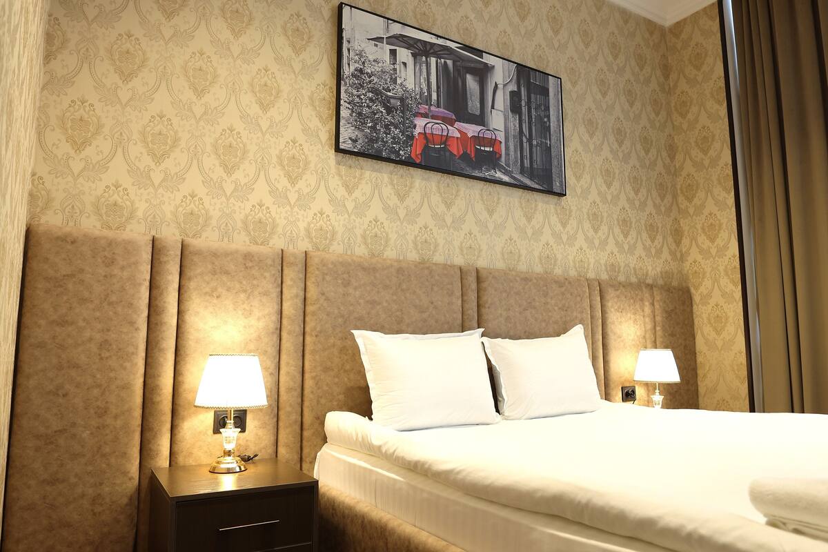 Une chambre d’hôtel avec un grand lit, deux lampes de chevet, une tête de lit, un tableau encadré au mur et une table de chevet.