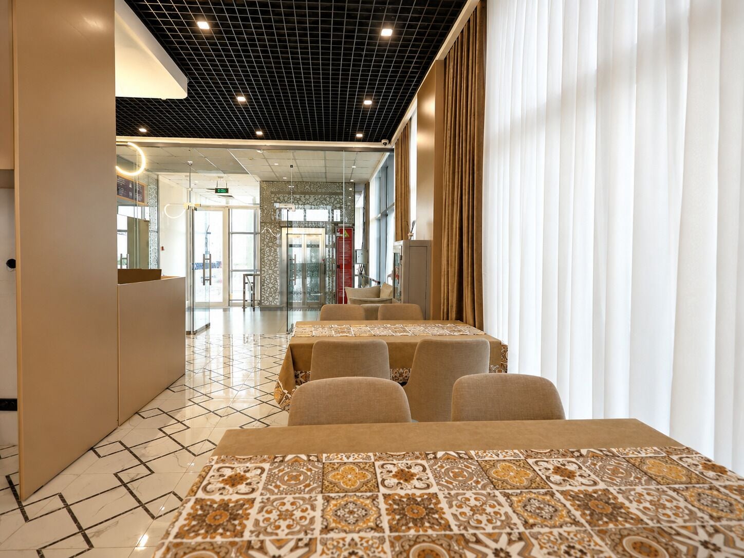 Un hall de hotel con suelo de baldosas, una recepción y un área de estar con mesas y sillas.