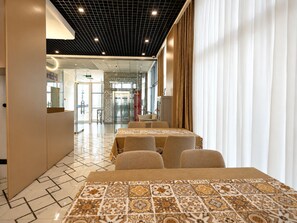 Un hall de hotel con suelo de baldosas, una recepción y un área de estar con mesas y sillas.