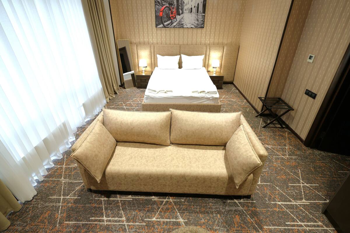 Une chambre d’hôtel avec un lit, un canapé, un tableau au mur et une moquette à motifs.