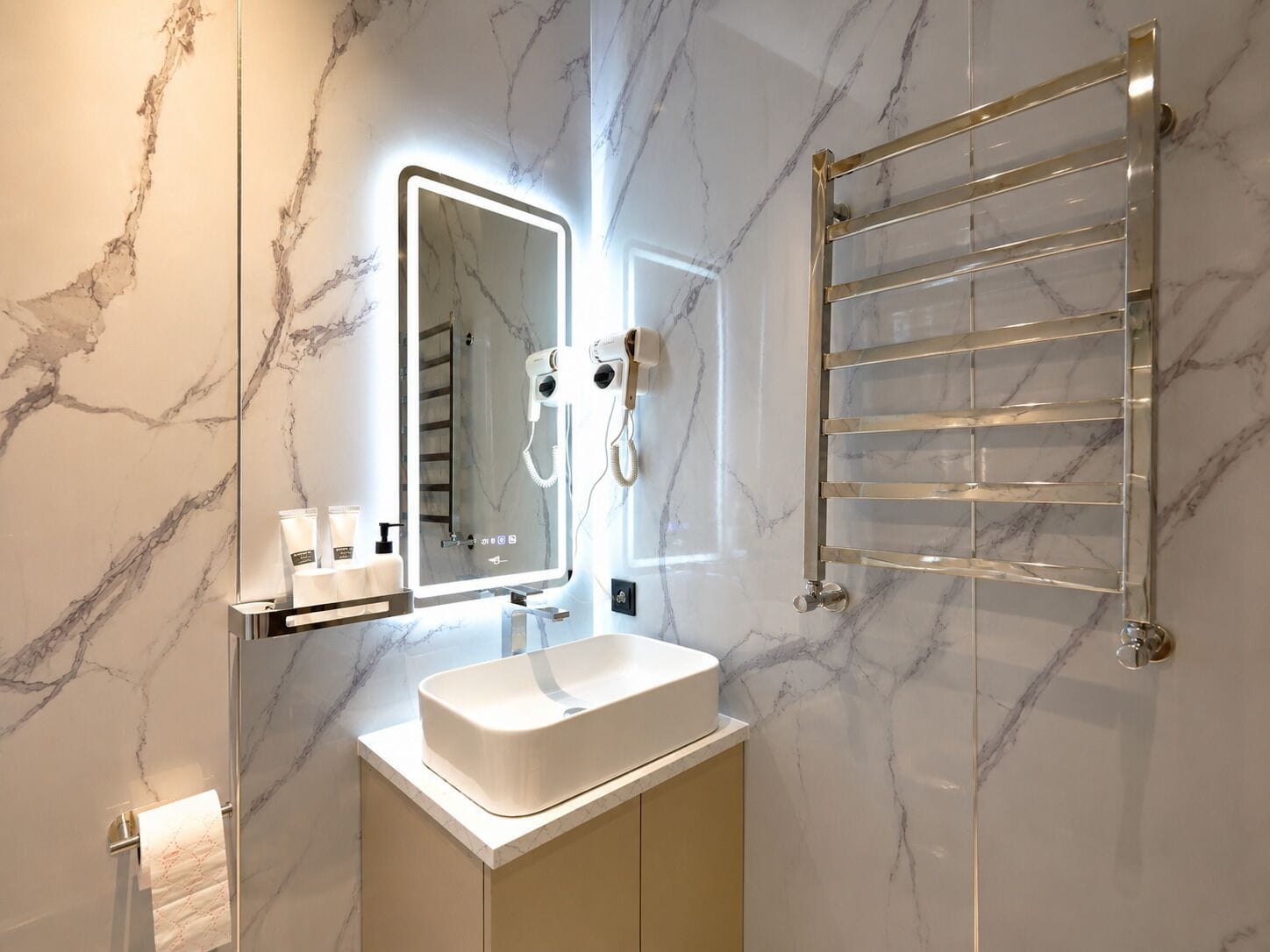 A bathroom with a marble wall, a sink, a mirror, a towel rack, and a hairdryer.