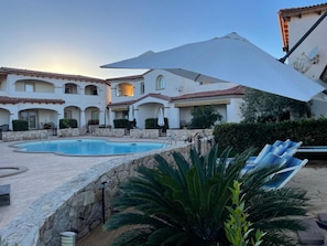 A pool area with a stone wall, lounge chairs, and a large umbrella. - Turquoise&Wood Stylish House – Modern Apartment with Pool View in Limpiddu (Limpiddu)