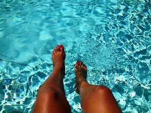 Piernas de alguien en una piscina cristalina con ondulaciones y reflejos visibles.