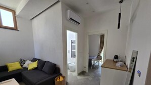 A compact living space with a sofa, a small table, a kitchen area with a refrigerator, and a bathroom visible through an open door. - N haidea - AgriFarm e B&B  (Lettere)