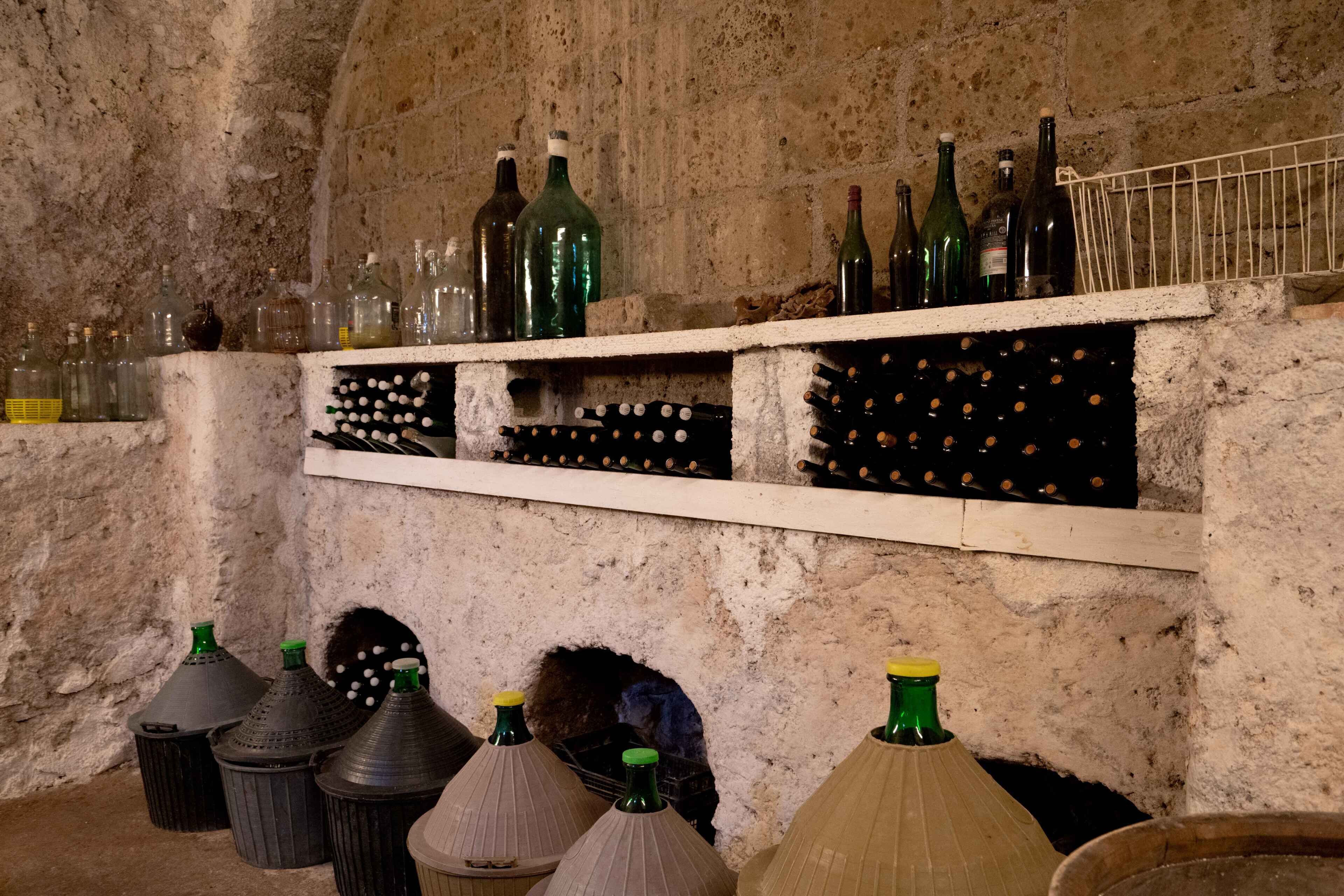 Una bodega con botellas y estanterías para vino frente a una pared con textura.