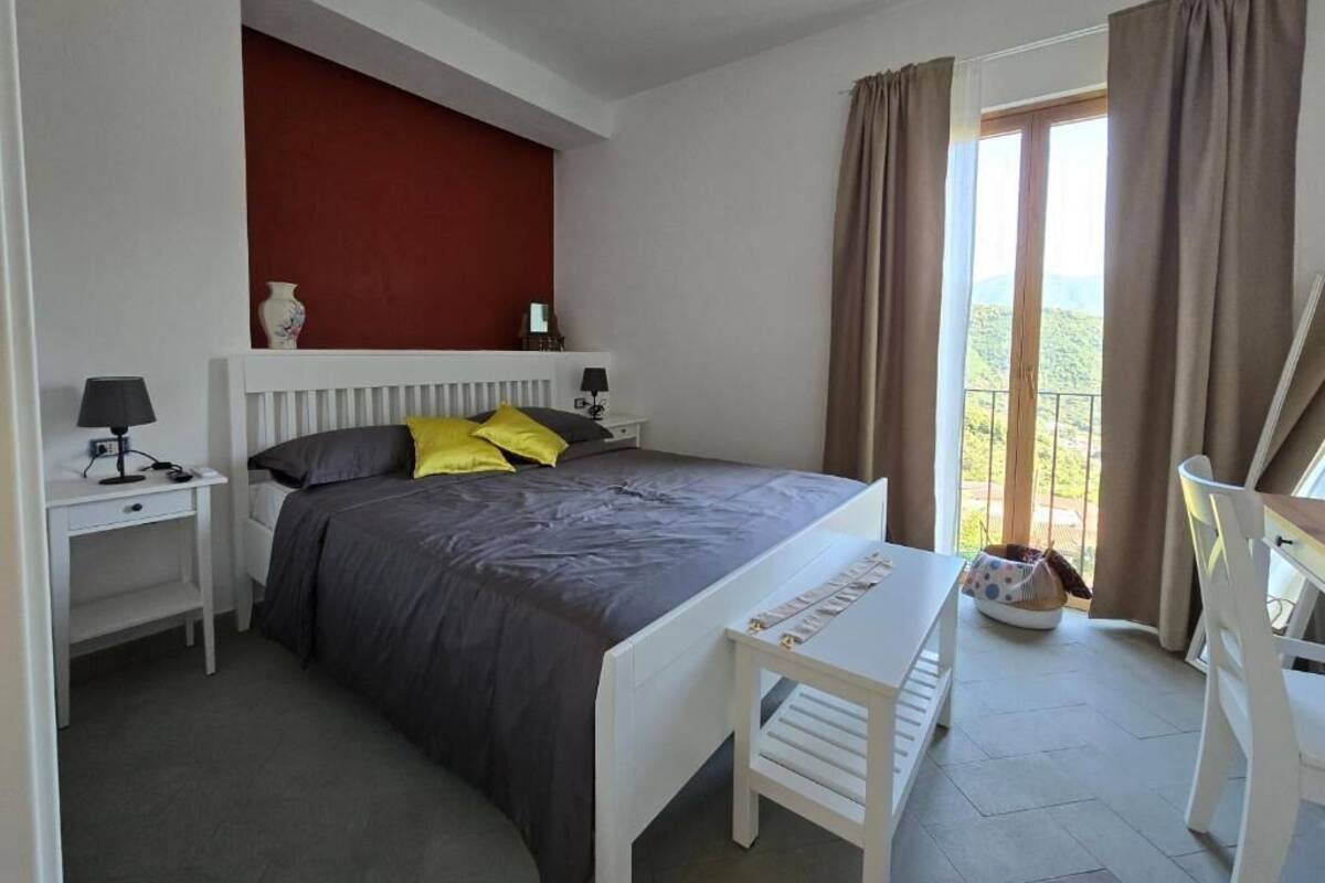 A bedroom with a bed, bedside tables, a desk, a chair, and a view through a window.