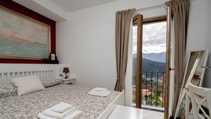 A bedroom with a bed, a nightstand, a lamp, a painting, and a view through a window. - N haidea - AgriFarm e B&B  (Lettere)