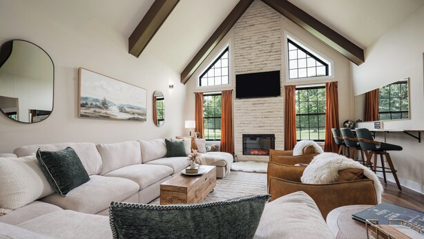A modern living room with a sectional sofa, a fireplace, and large windows. - Alpine Ridge | Brand New Build | Sleeps 16 (Boyne City)