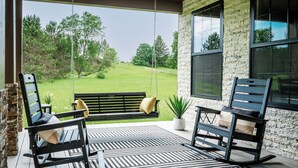 A porch with two rocking chairs, a bench, and a potted plant. - Alpine Ridge | Brand New Build | Sleeps 16 (Boyne City)