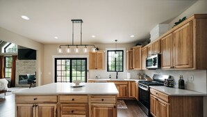 A spacious kitchen with wooden cabinets, a large island, and a modern stove. - Alpine Ridge | Brand New Build | Sleeps 16 (Boyne City)