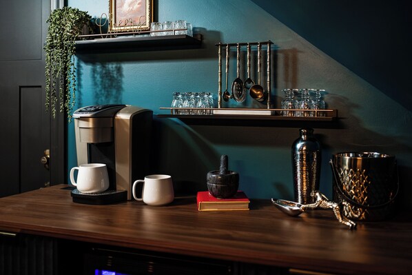A coffee machine, two cups, a book, a plant, and kitchen utensils on a wooden table. - Alpine Ridge | Brand New Build | Sleeps 16 (Boyne City)