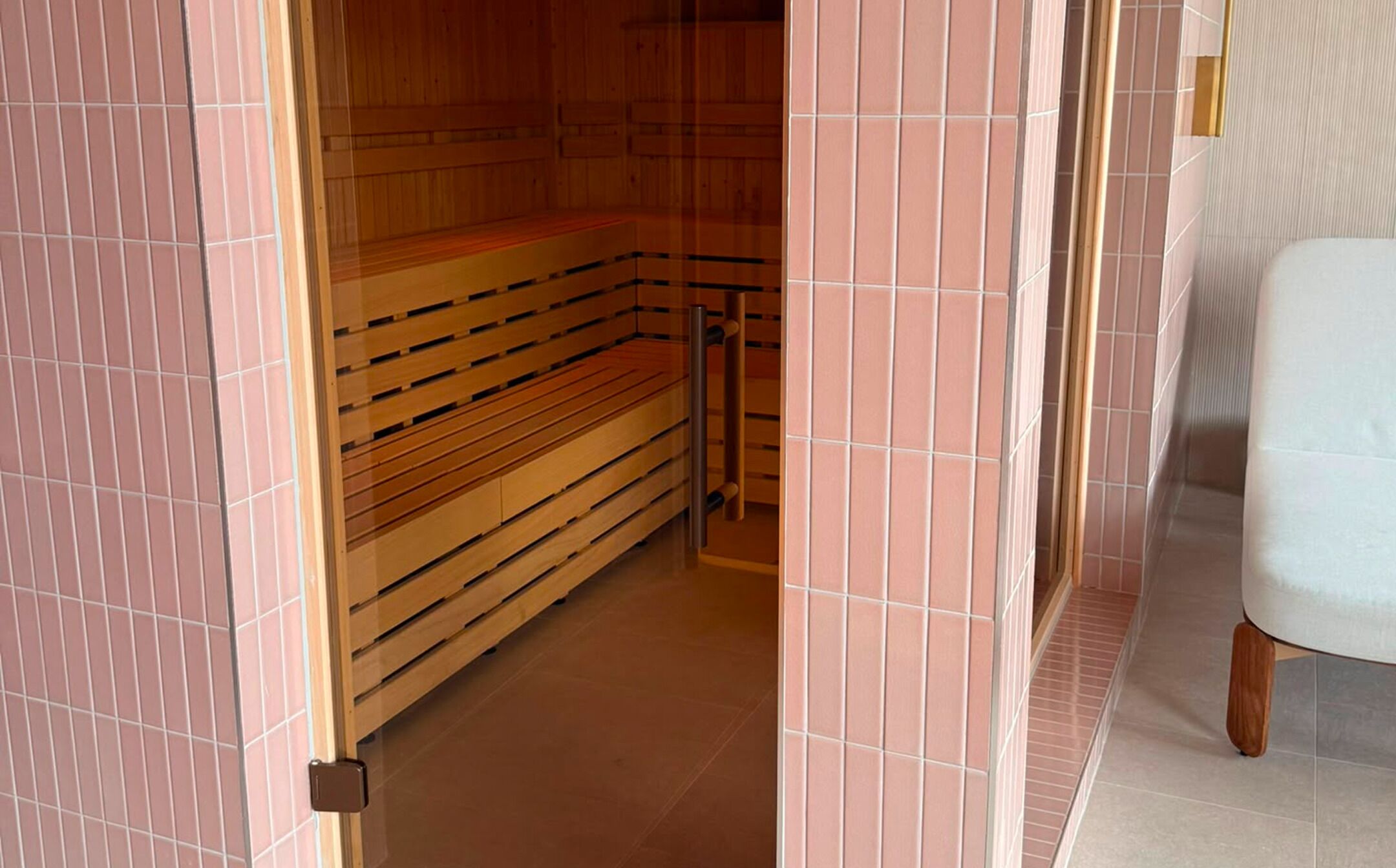 A sauna room with wooden benches, a metal rack, and pink-tiled walls.