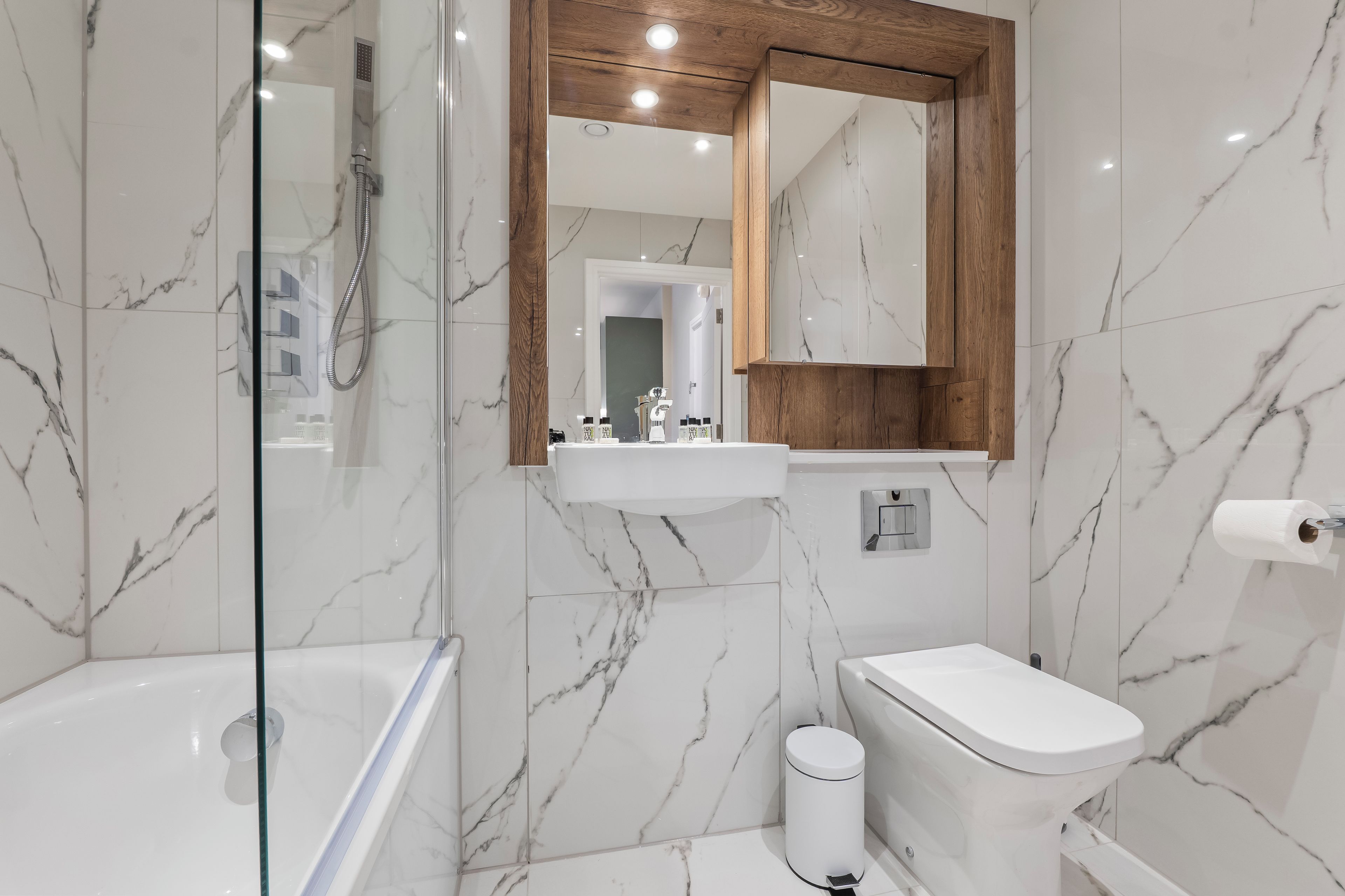 A modern bathroom with a glass-enclosed shower, a white toilet, and a marble-tiled wall.