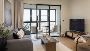 A modern living room with a sofa, armchairs, a coffee table, a TV, and a sliding glass door leading to a balcony. - StayCozy Apartments in Birmingham (Birmingham)