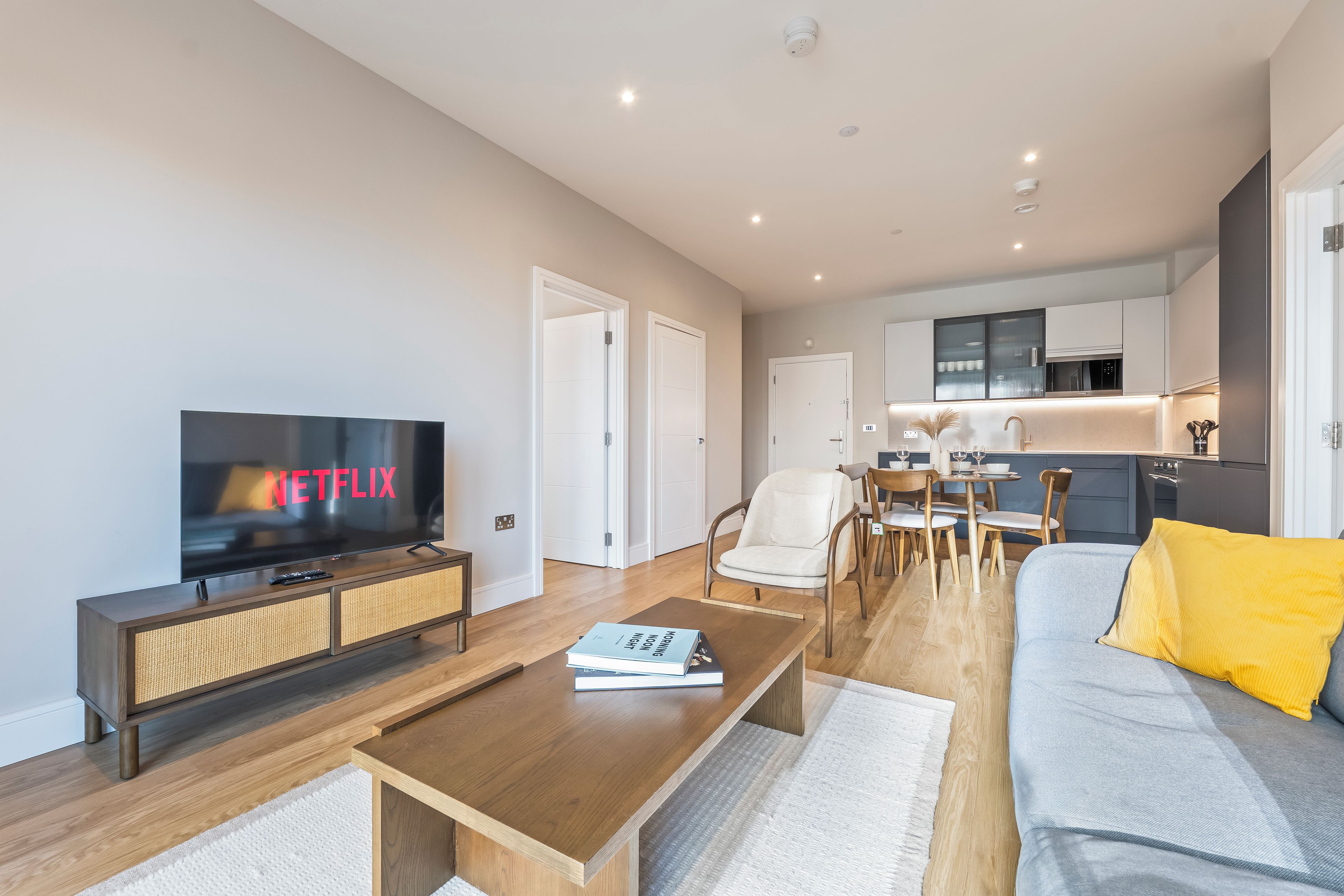 A modern living room with a flat-screen TV, a coffee table, a sofa, and a dining area with chairs and a table.