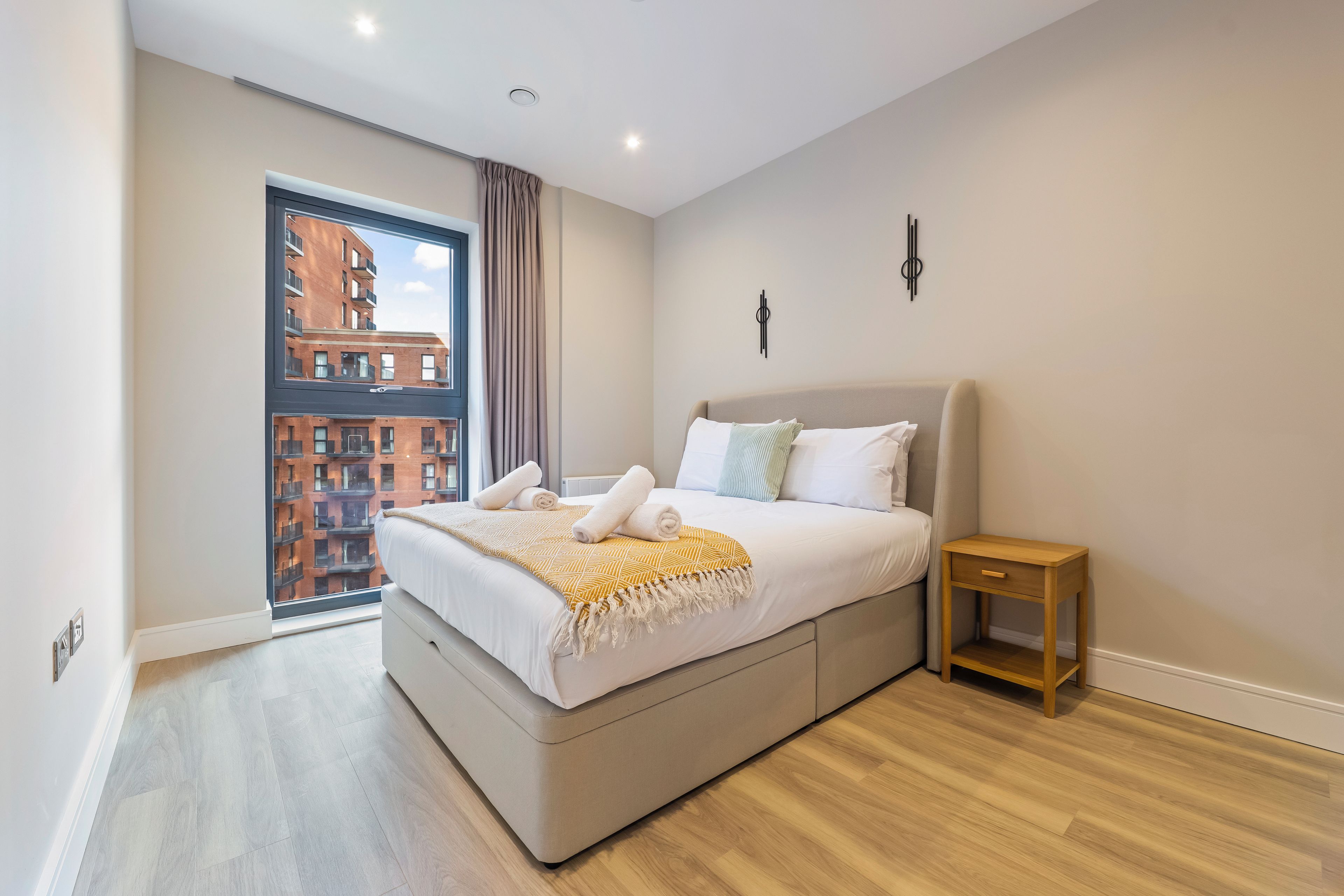 A modern bedroom with a large bed, a nightstand, and a view of a building through a window.