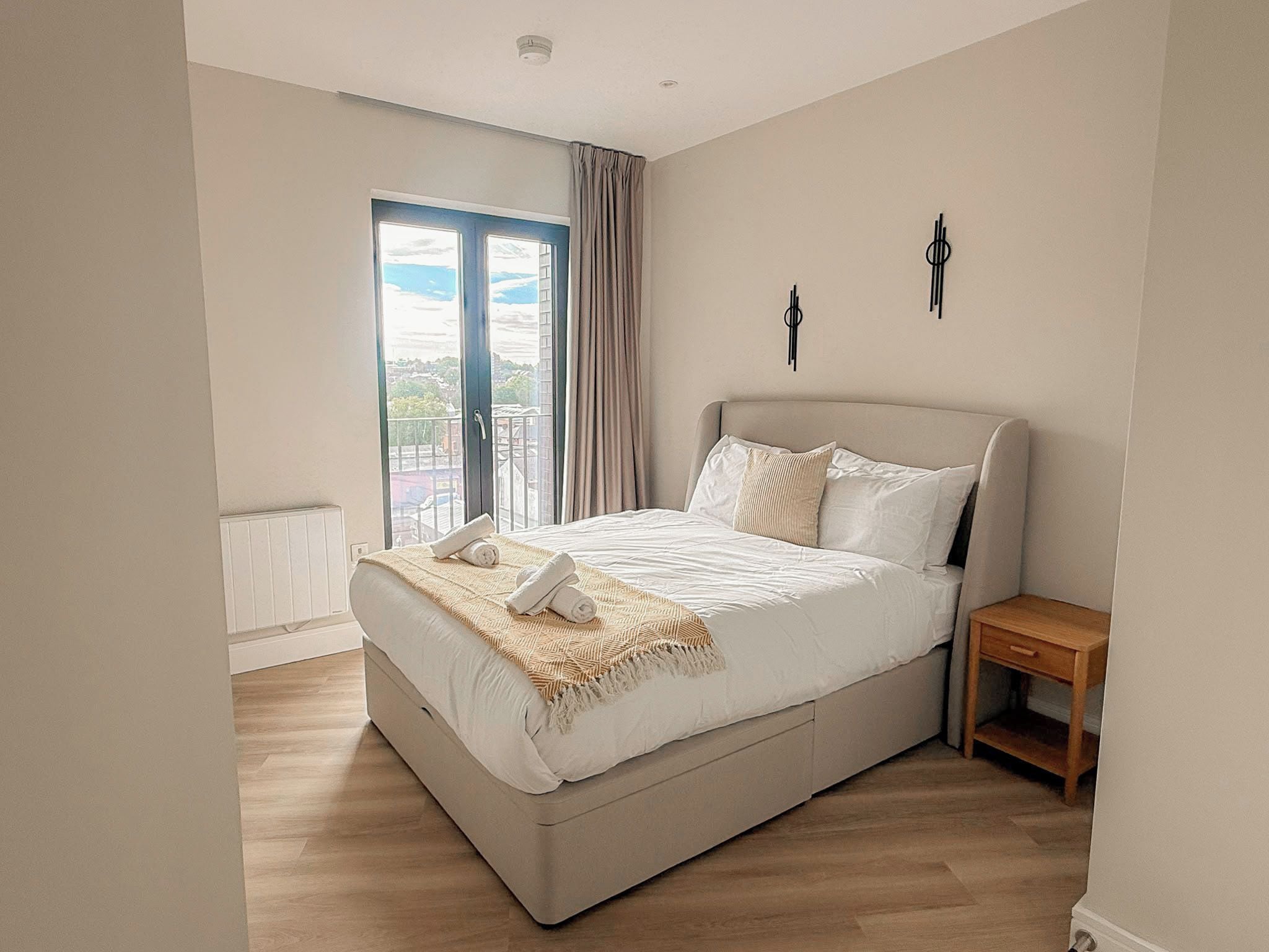 Un dormitorio con una cama grande, una mesita de noche, una ventana con cortinas y vistas al exterior.