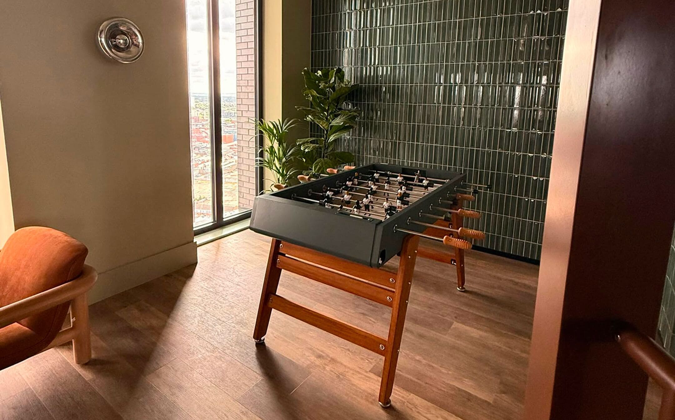 Une pièce avec une table de baby-foot, une chaise en bois et une vue sur l’extérieur par une fenêtre.