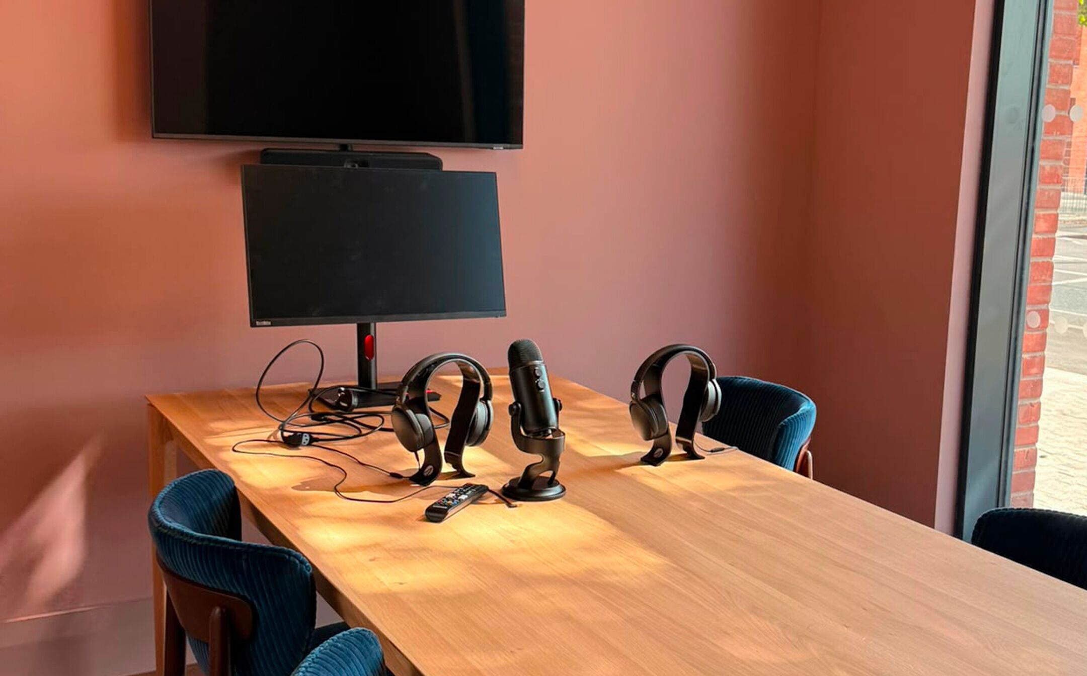 A conference room with a wooden table, two blue chairs, a black monitor, and a microphone.