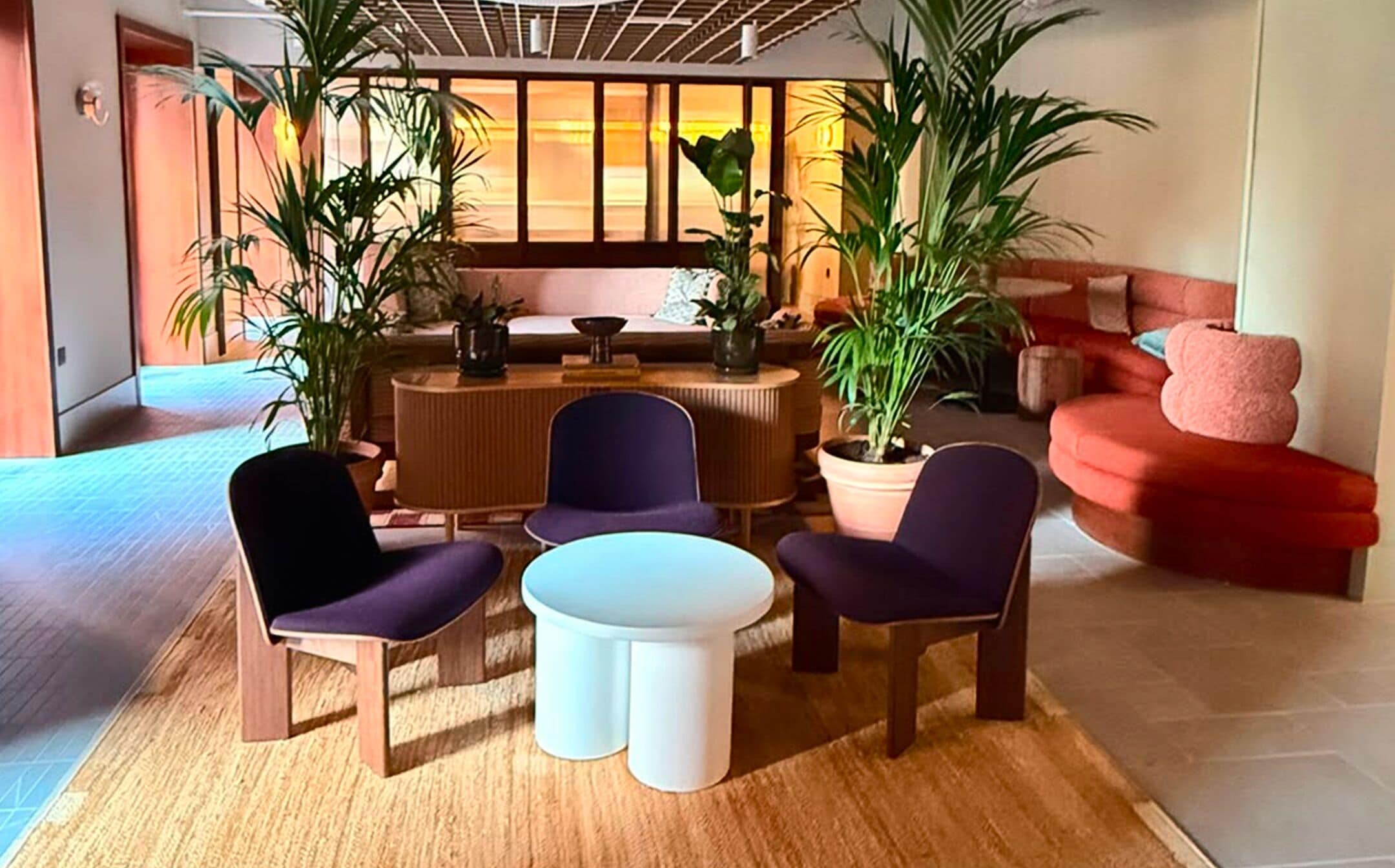 Una sala de estar moderna con una mesa redonda, sillas moradas, un sofá rojo y varias plantas en macetas.