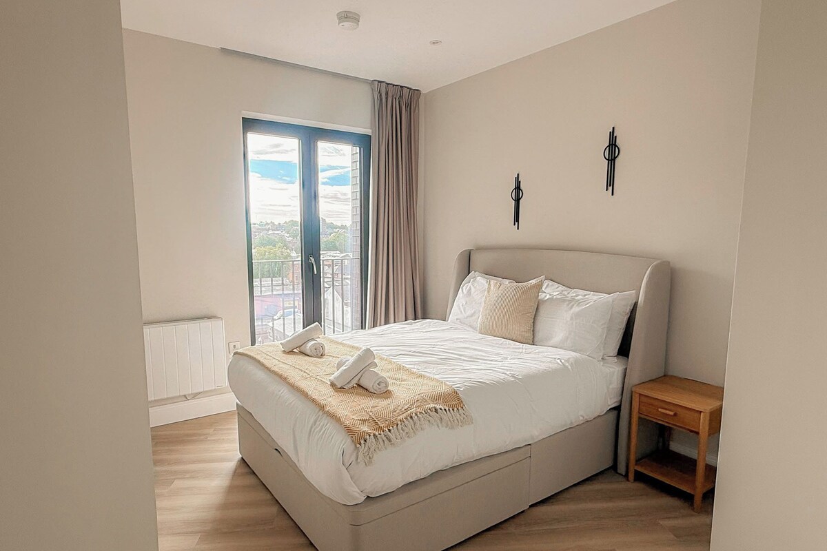 A bedroom with a large bed, a nightstand, a window with curtains, and a view of the outside.