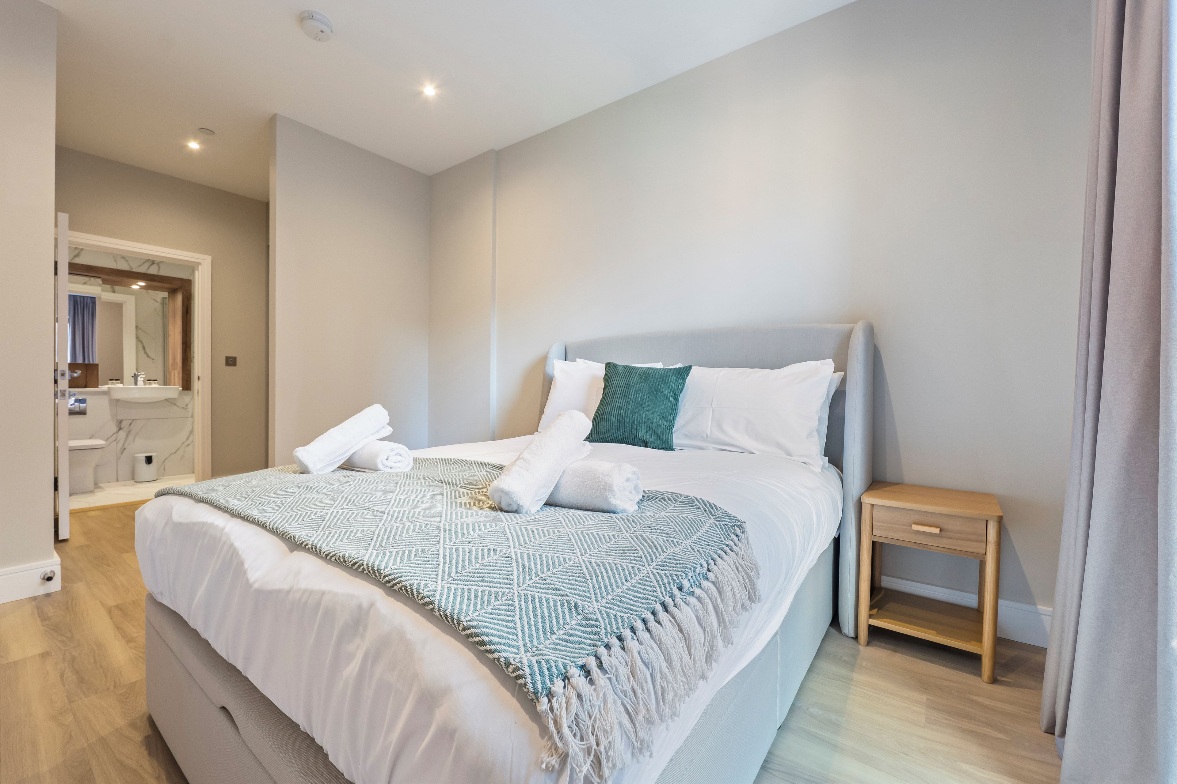 A hotel room with a bed, a bedside table, a mirror, and a bathroom visible through an open door.