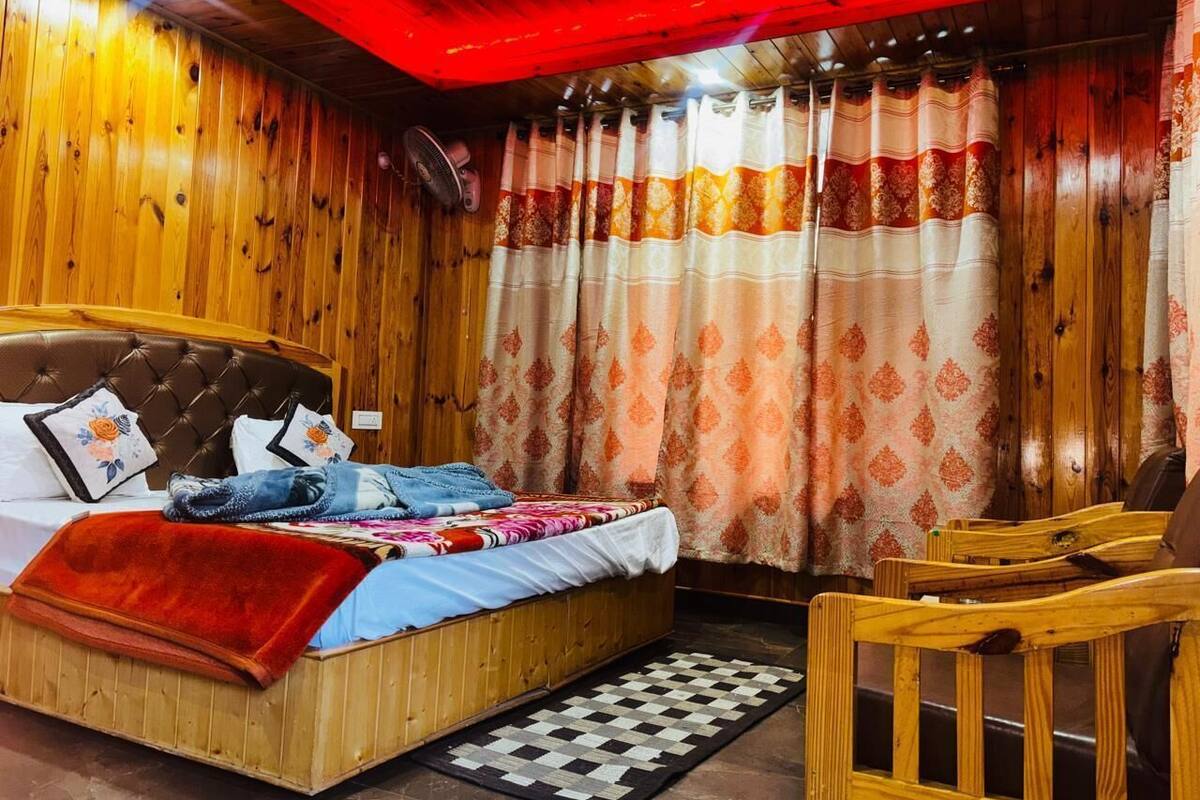 Habitación con paneles de madera, una cama, una silla, un ventilador y cortinas.