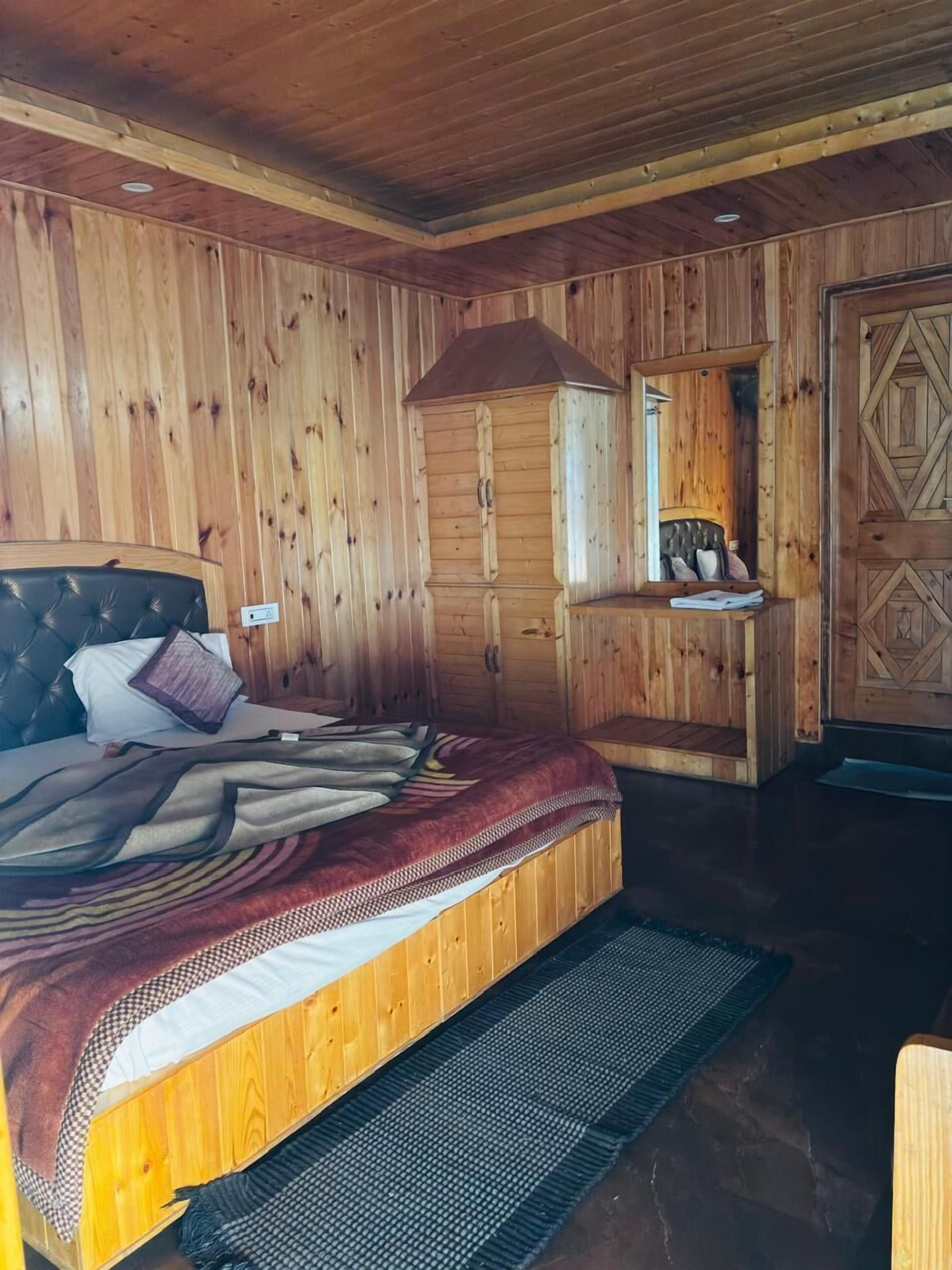 A wooden-paneled room with a bed, a small desk, and a mirror.